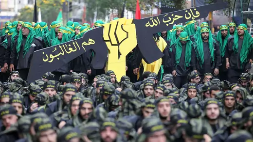 A crowd of Hezbollah supporters surrounds a giant model of a fist holding a gun. 