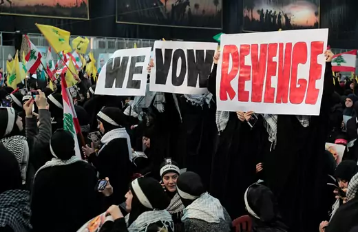 Hezbollah supporters hold signs that say "we vow revenge" and wave the Hezbollah and Lebanese flags.