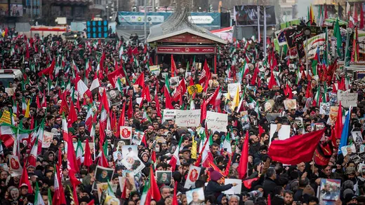 People hold flags and signs during a funeral procession in Iran for Qasem Soleimani.