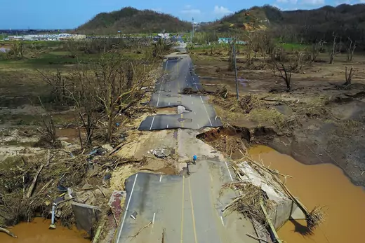 A man rides his bicycle through a damaged road in Puerto Rico. 