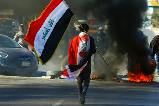 A demonstrator carries an Iraqi flag as he walks near burning tires, during ongoing anti-government protests in Najaf, Iraq January 12, 2020.