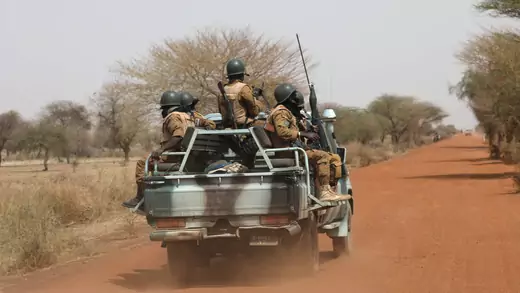 Armed Burkinabe soldiers ride in a truck, facing to the left and the right, as it drives down a dirt road during a patrol in the Sahel region of Burkina Faso.