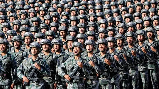 Dozens of Chinese soldiers march in lines, holding guns and wearing camouflage, in preparation for a military parade. 