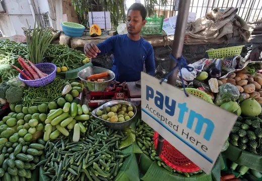 A vendor weighs vegetables next to an ad for Paytm, a digital payments firm, at a roadside market in Mumbai.