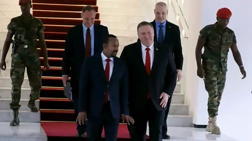 U.S. Secretary of State Mike Pompeo, in a dark suit with a red tie, walks with Ethiopian Prime Minister Abiy Ahmed, in a navy suit with a red tie, walks down white marble stairs with a red carpet at the Prime Minister office after a meeting in Addis Ababa, Ethiopia. They are followed by two men in suits, and flanked by two armed Ethiopian guards in red berets and military fatigues.