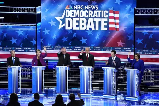 Democratic candidates raise their hand to speak while they stand behind podiums at the Democratic debate on Wednesday, February 19. 