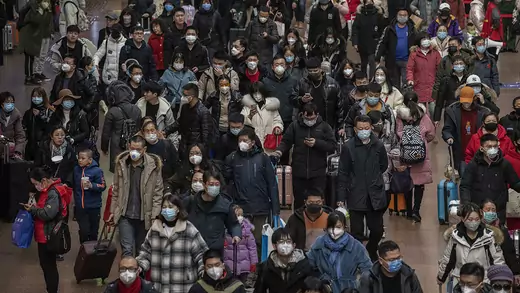 Dozens of people wear face masks and carry suitcases while walking through a Beijing railway station.