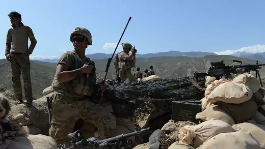 Several U.S. soldiers stand in a pit on a mountain fortified with sandbags and guns in Afghanistan.