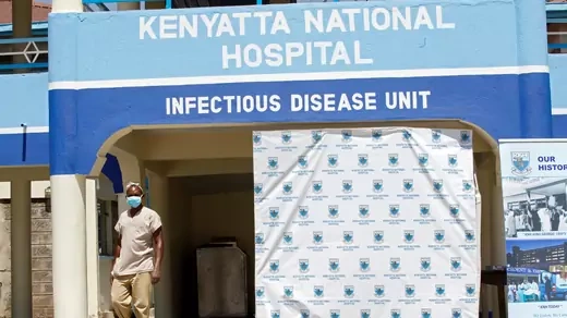 A worker wearing tan clothes and a blue medical mask walks outside the coronavirus isolation facility at the Mbagathi Hospital in Nairobi, Kenya, on March 15, 2020. 