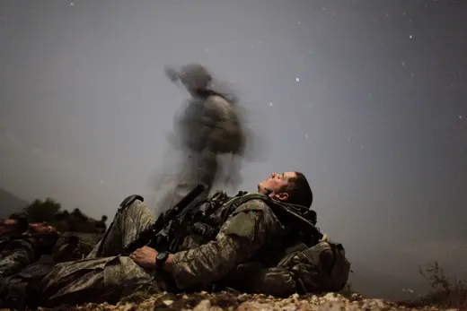 A U.S. soldier of 2-12 Infantry 4BCT-4ID Task Force Mountain Warrior takes a break while another soldier walks by, out of the camera's focus, during a night mission near Honaker Miracle camp at the Pesh valley of Kunar Province, August 12, 2009.