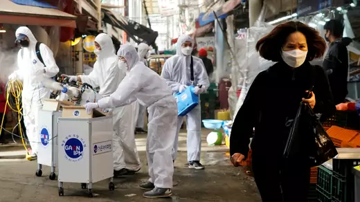 A woman wearing a mask to prevent contracting the coronavirus reacts as employees from a disinfection service company sanitize a traditional market in Seoul, South Korea, on February 26, 2020.