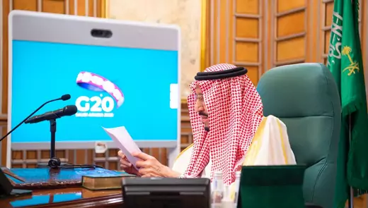 Saudi King Salman bin Abdulaziz speaks via video link as he sits at a desk, with a monitor displaying "G20" in the background. 