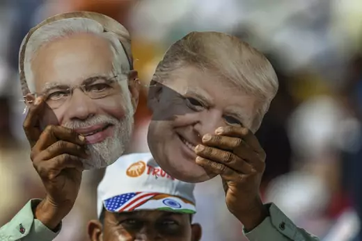 An Indian man in a white hat holds up masks of Narendra Modi and Donald Trump