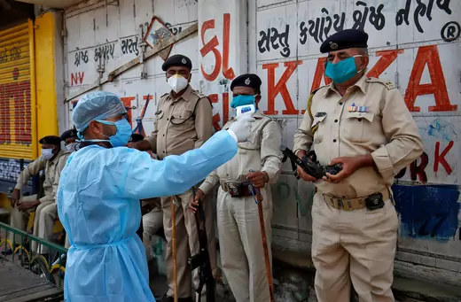 A paramedic measures the temperature of a police officer in Ahmedabad, India during a 21-day nationwide lockdown, April 9, 2020. 