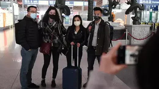 Four people wear face masks and pose for a photo in the Beijing airport. 