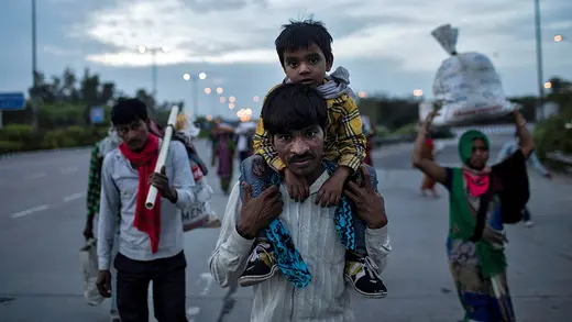 A man carries his son on his shoulders as they walk down an empty road.