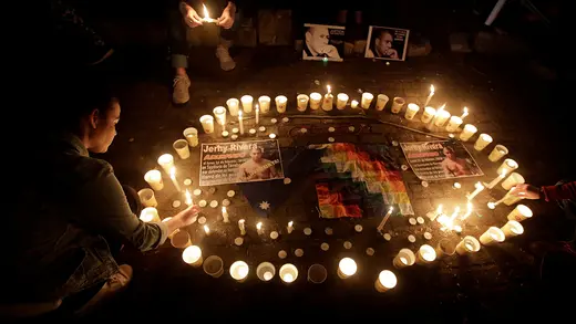 A nighttime photo looking down on a circle of candles with textiles and signs in the middle of it. Two people appear nearby.