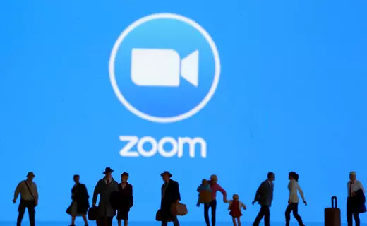 Small toy figures are seen in front of diplayed Zoom logo.