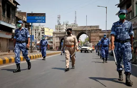 Two columns of soldiers in blue uniforms patrol a street, with an officer in a beige uniform walking between them.