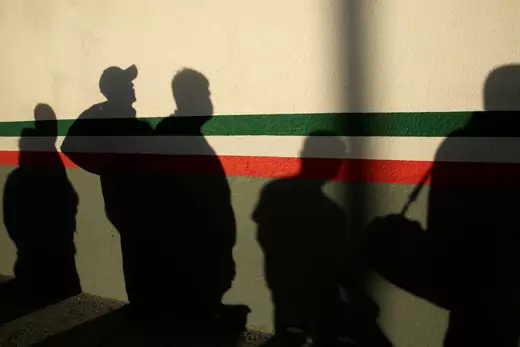 Mexican immigrants cast shadows on a striped National Institute of Migration (INM) building in Ciudad Juarez, Mexico