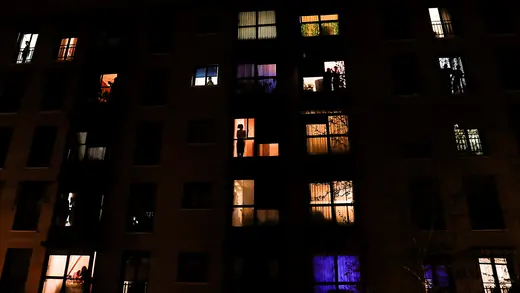 People look outside their apartment windows at night to thank health-care workers during the coronavirus pandemic