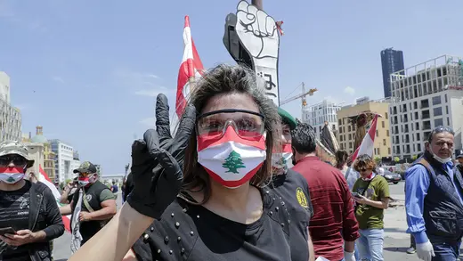 A woman wearing a face mask resembling Lebanon's flags hold her hand in a peace sign during Beirut protest.
