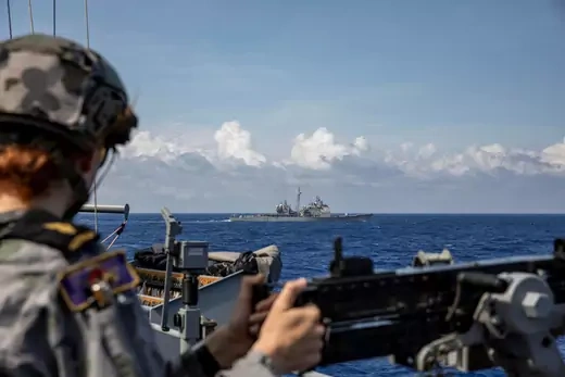 A member of the Australian Navy stands behind a gun while watching the USS Bunker Hill move into position during a joint U.S.-Australia training exercise in the South China Sea on April 14, 2020.