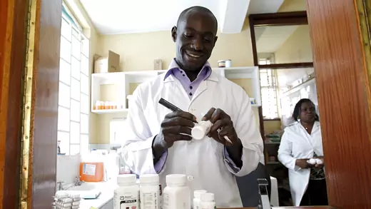 Michael Otieno, a pharmacist, smiles as he marks with a pen a bottle of anti-retroviral (ARV) drugs at the Mater Hospital in Kenya's capital Nairobi, on September 10, 2015. He is wearing a white doctor's coat and is framed by a wooden booth.