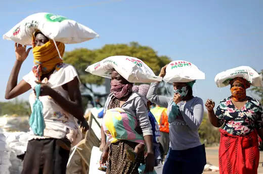 Women carry bags of maize as people queue to receive food aid amid the spread of the novel coronavirus, near Pretoria, South Africa, on May 20, 2020.