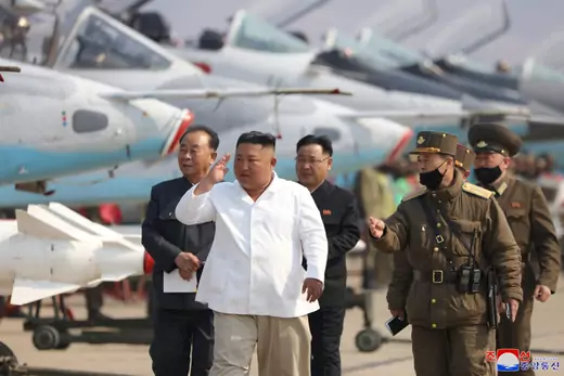 Kim Jong-un walks with men in military uniforms in front of military planes. 
