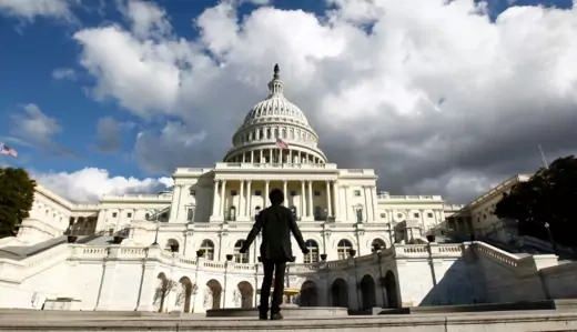 Tourist, dressed in black, stands in front of U.S. Capitol building. 
