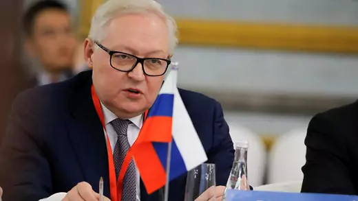 Russian Deputy Foreign Minister sits at a table with Russian flag displayed