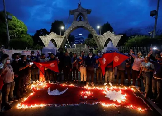 People gathering at dusk in a park around a Nepali flag surrounded by candles on the ground