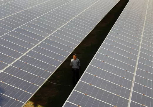 A private security guard walks between rows of photovoltaic solar panels inside a solar power plant at Raisan village near Gandhinagar, in the western Indian state of Gujarat, February 11, 2014.