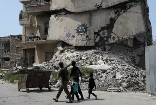 Two adults and two children walk by a destroyed building on which images of the novel coronavirus have been spray painted in Idlib, Syria.
