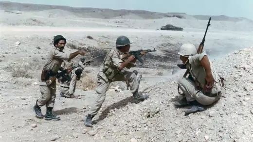 Three soldiers stand in the desert with guns pointed