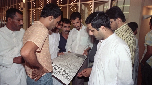 One man holds a newspaper with an article about the downed Iranian air jet, which several other men are looking at.