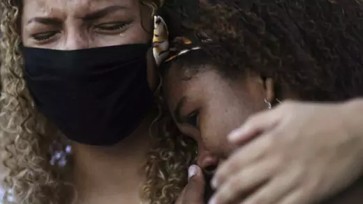 Two Brazilian women cry, one wears a face mask to protect herself from the coronavirus. 