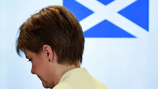 Scotland's First Minister Nicola Sturgeon stands in front of a blue Scottish flag