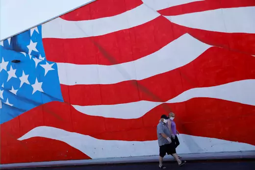 People wearing masks walk past an American flag painted on a building during the outbreak of the coronavirus disease (COVID-19) in Ocean Beach, California, U.S.