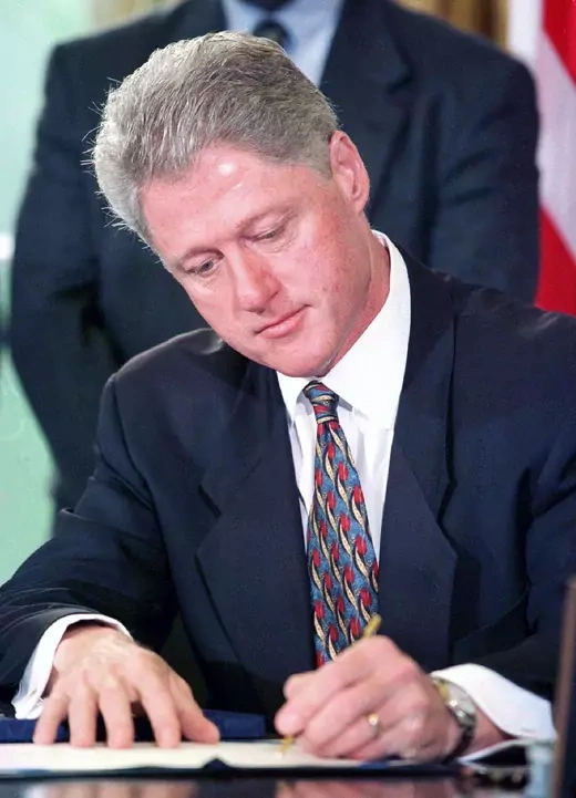 President Bill Clinton signs a law while seated in the Oval Office