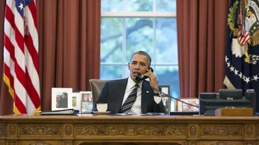 Barack Obama speaks on the phone while seated in the Oval Office