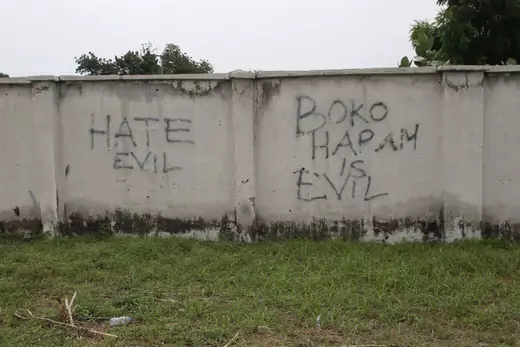 Black graffiti is shown on a gray wall in Borno, Nigeria. The graffiti says "Hate Evil," as well as "Boko Haram is Evil"