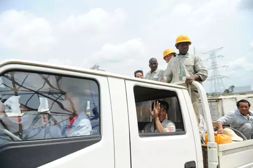 Workers from China and Burkina Faso employed by Sinohydro standing on back of truck driven by chinese workers.
