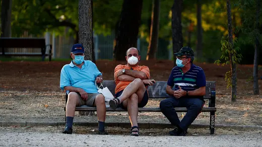 Three men wearing protective face masks sit on a bench at Las Cruces Park in Madrid, Spain, amid the coronavirus pandemic, July 28, 2020.