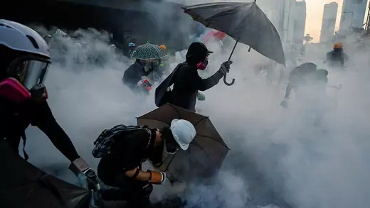 Anti-government protesters at a demonstration, protect themselves with umbrellas among tear gas near Central Government Complex in Hong Kong
