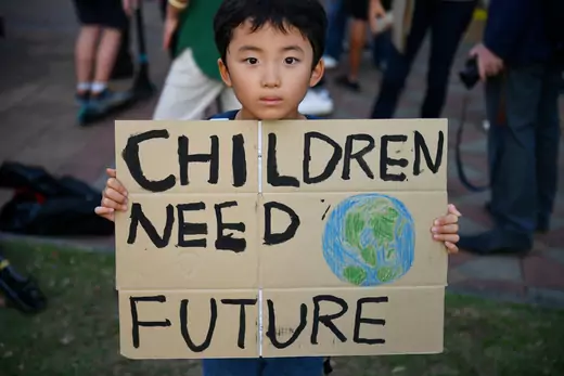 A child holds a sign that says "Children need future" at a climate change protest in Thailand.
