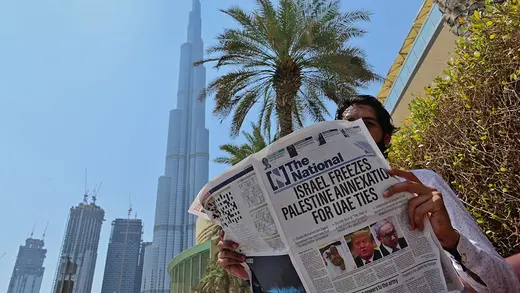A man near the Burj Khalifa in Dubai reads a newspaper with the headline "Israel Freezes Palestine Annexation for UAE Ties"