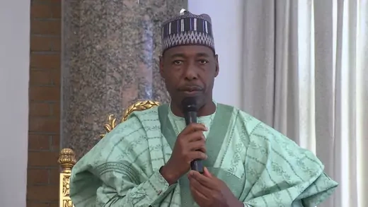 Nigerian man, the governor of Borno State, speaks into microphone wearing green traditional clothing
