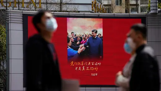 People wearing masks walk by a display showing an image of Xi Jinping smiling.